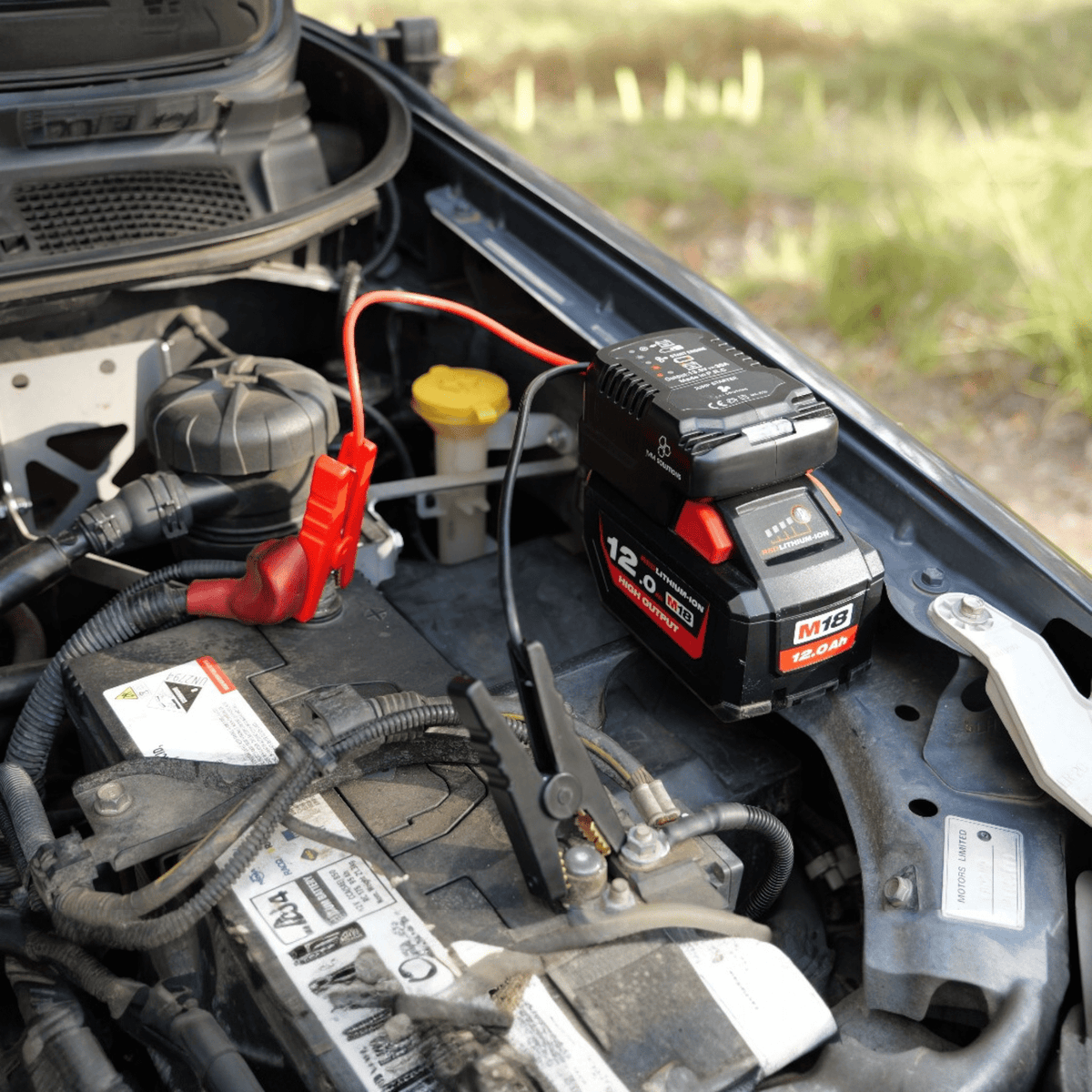 Milwaukee-compatible 18V Jump Starter: clamps connected to a vehicle battery in the engine bay